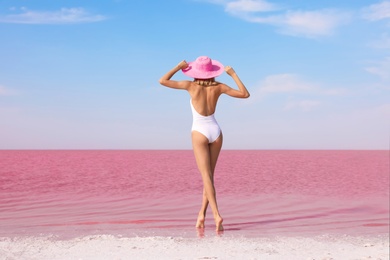 Beautiful woman in swimsuit posing near pink lake on sunny day