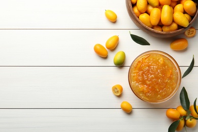 Delicious kumquat jam in bowl and fresh fruits on white wooden table, flat lay. Space for text