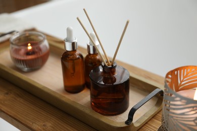 Wooden tray with cosmetic products, reed air freshener and burning candles on bath tub, closeup