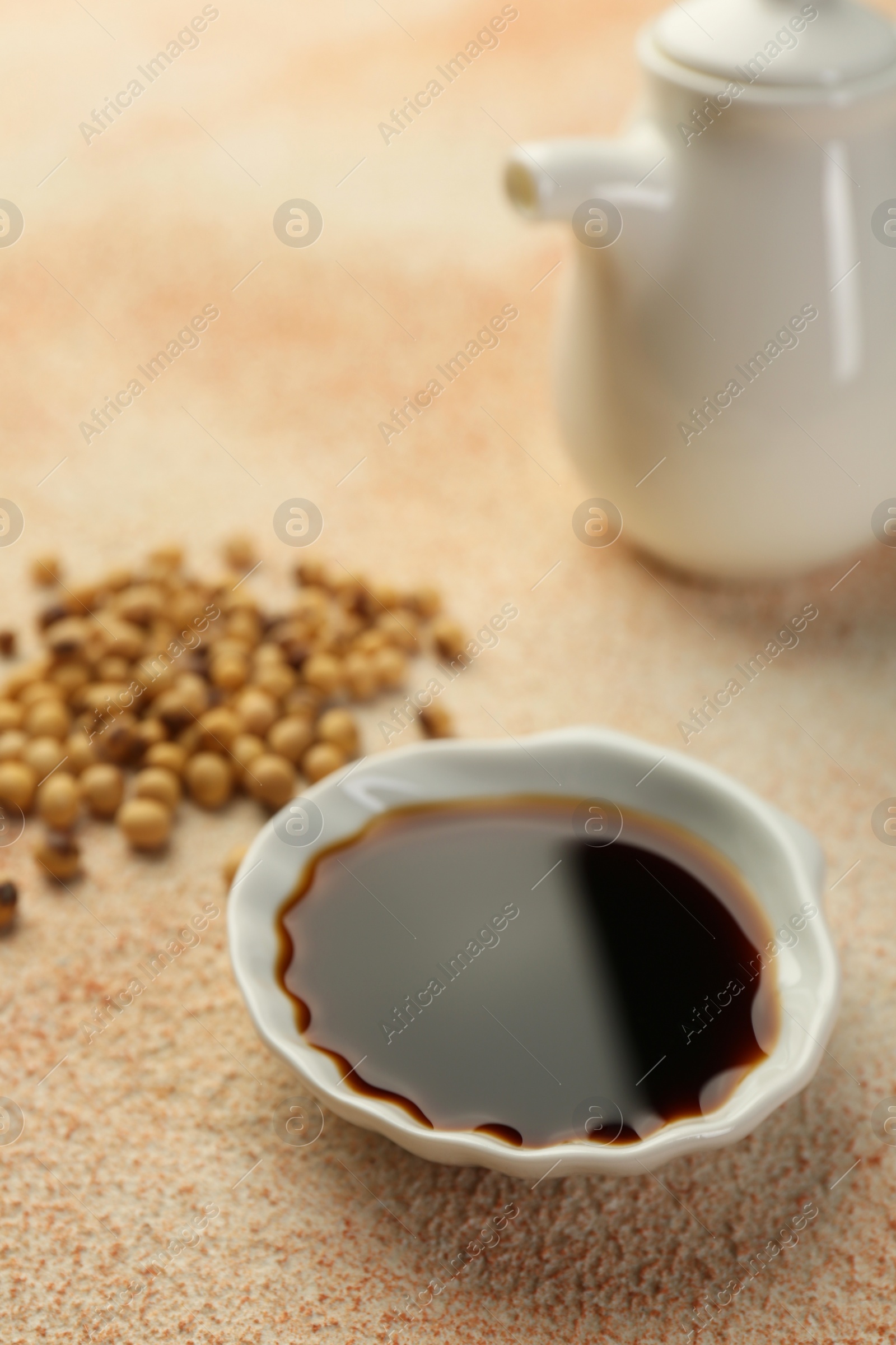 Photo of Soy sauce in bowl and beans on beige textured table