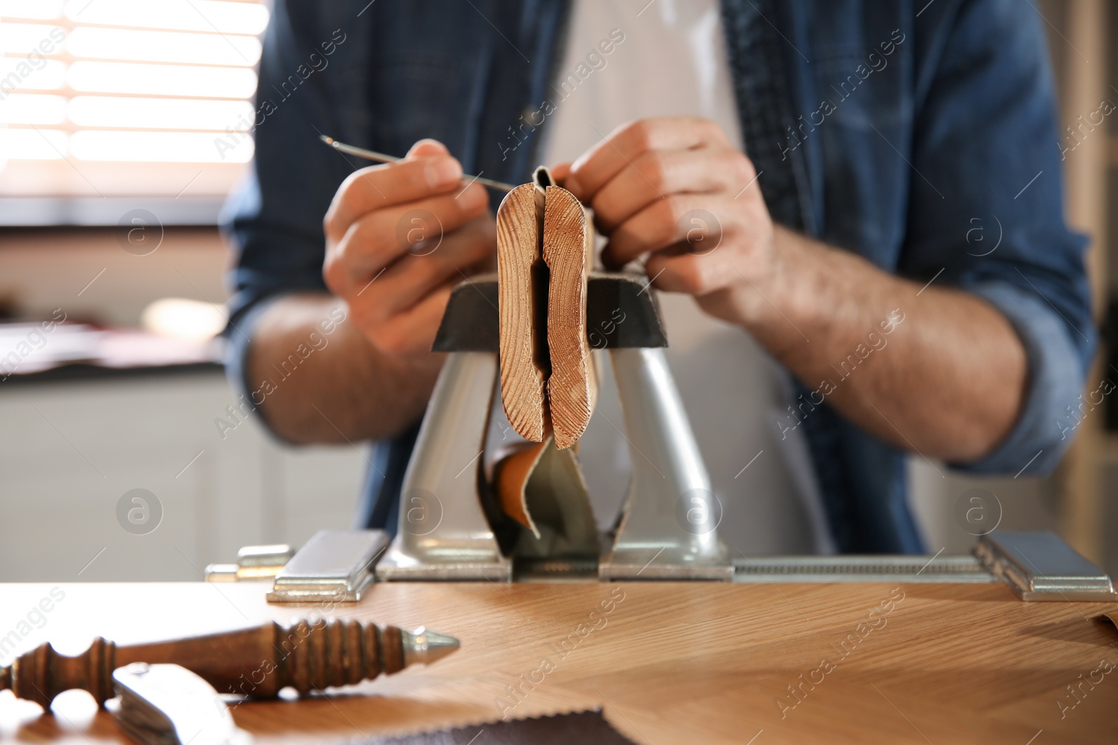 Photo of Man sewing piece of leather in workshop, closeup