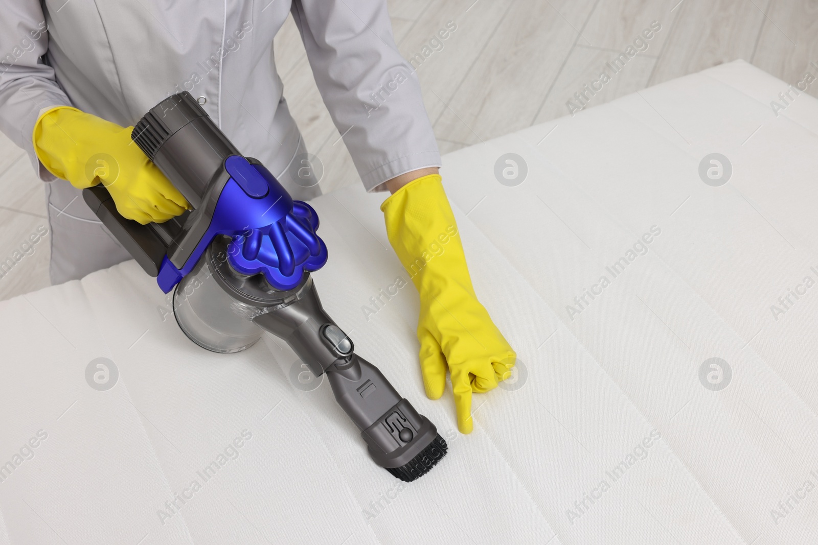 Photo of Woman in gloves disinfecting mattress with vacuum cleaner indoors, closeup. Space for text