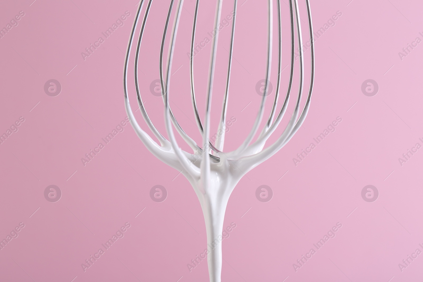 Photo of Whisk with whipped cream on pink background, closeup