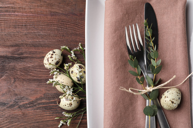 Festive Easter table setting with quail eggs and floral decor on wooden background, flat lay
