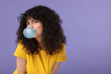 Beautiful young woman blowing bubble gum on purple background. Space for text