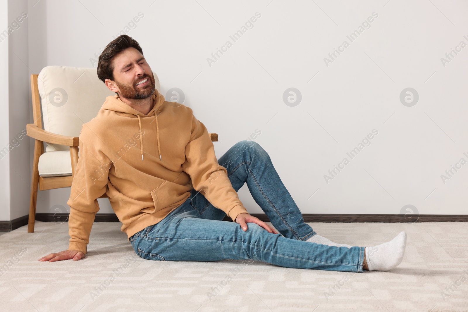 Photo of Man suffering from leg pain on carpet indoors