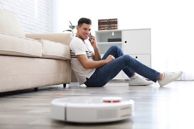 Photo of Man talking on phone while robotic vacuum cleaner doing his work at home