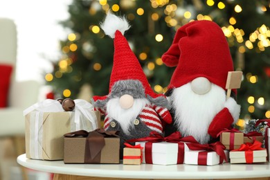 Photo of Funny Christmas gnomes and gift boxes on coffee table in room with festive decoration