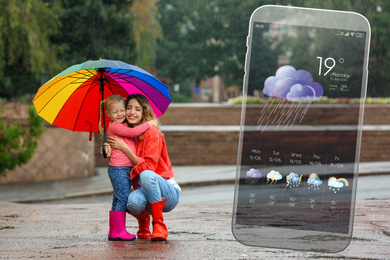 Image of Happy people under rain outdoors and smartphone with open weather forecast app 