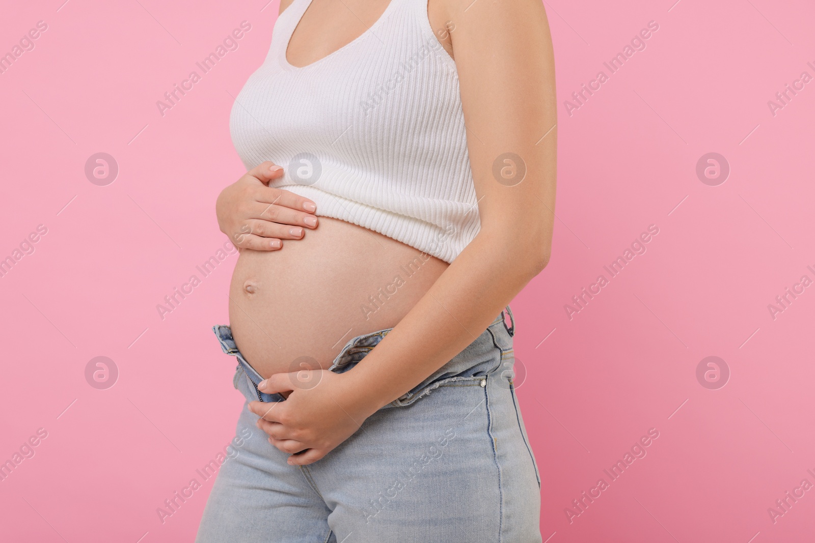 Photo of Pregnant woman in jeans on pink background, closeup