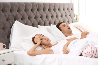 Photo of Young irritated woman lying on pillows in bed at home. Problem with snoring husband