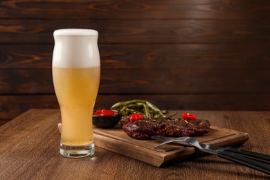 Glass of beer, delicious fried steak and sauce on wooden table. Space for text