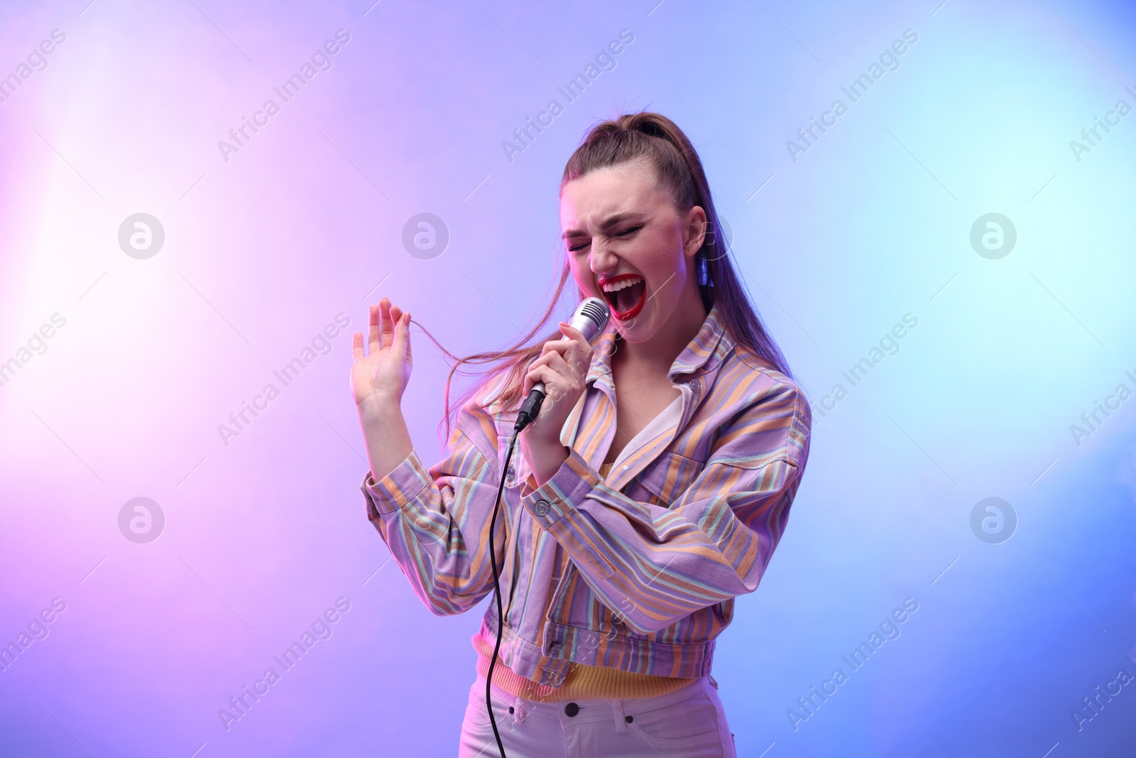 Photo of Emotional woman with microphone singing in color lights