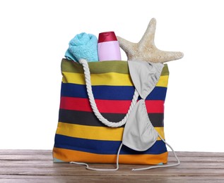 Photo of Stylish bag with starfish and other beach accessories on wooden table against white background