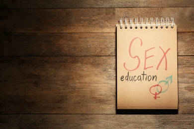 Photo of Notebook with phrase "SEX EDUCATION" and gender symbols on wooden background, top view. Space for text