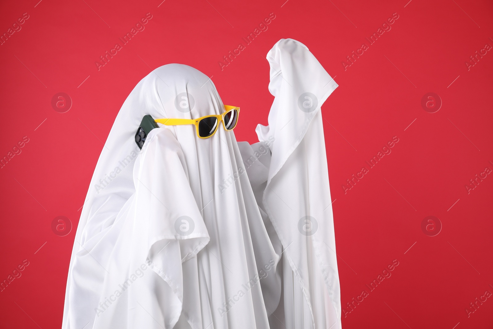 Photo of Person in ghost costume and sunglasses talking on smartphone against red background