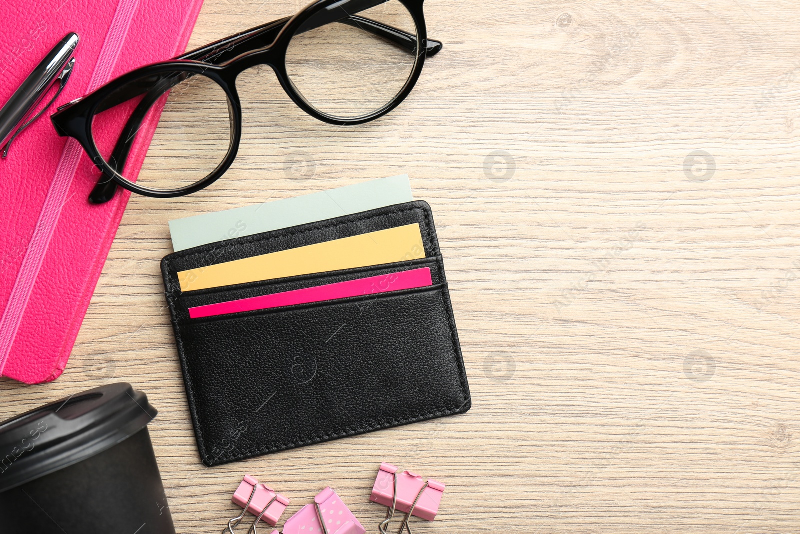 Photo of Leather business card holder with colorful cards, stationery, glasses and coffee on wooden table, flat lay. Space for text