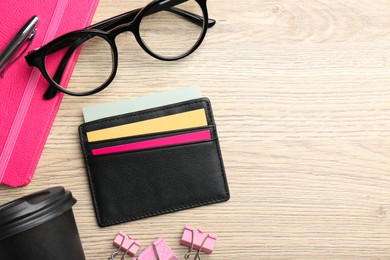 Leather business card holder with colorful cards, stationery, glasses and coffee on wooden table, flat lay. Space for text