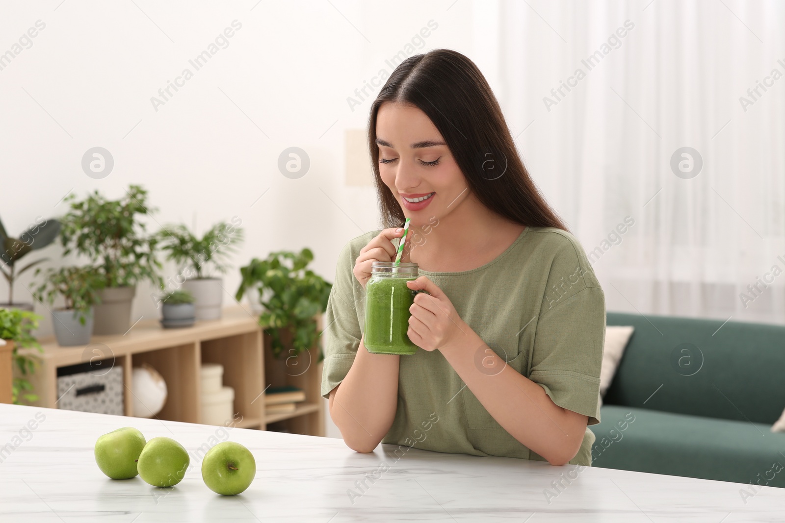 Photo of Beautiful young woman drinking delicious smoothie at home