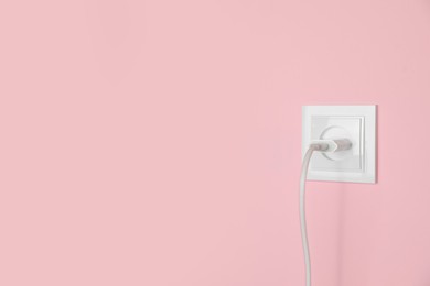 Photo of Charger adapter plugged into power socket on pink wall, space for text. Electrical supply