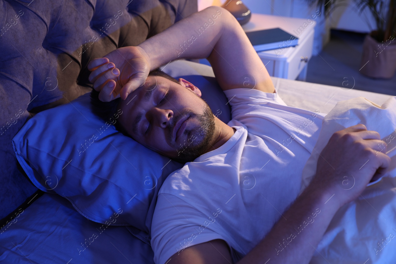 Photo of Handsome man sleeping on pillow in dark room at night. Bedtime