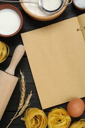 Blank recipe book and different ingredients on black wooden table, flat lay. Space for text