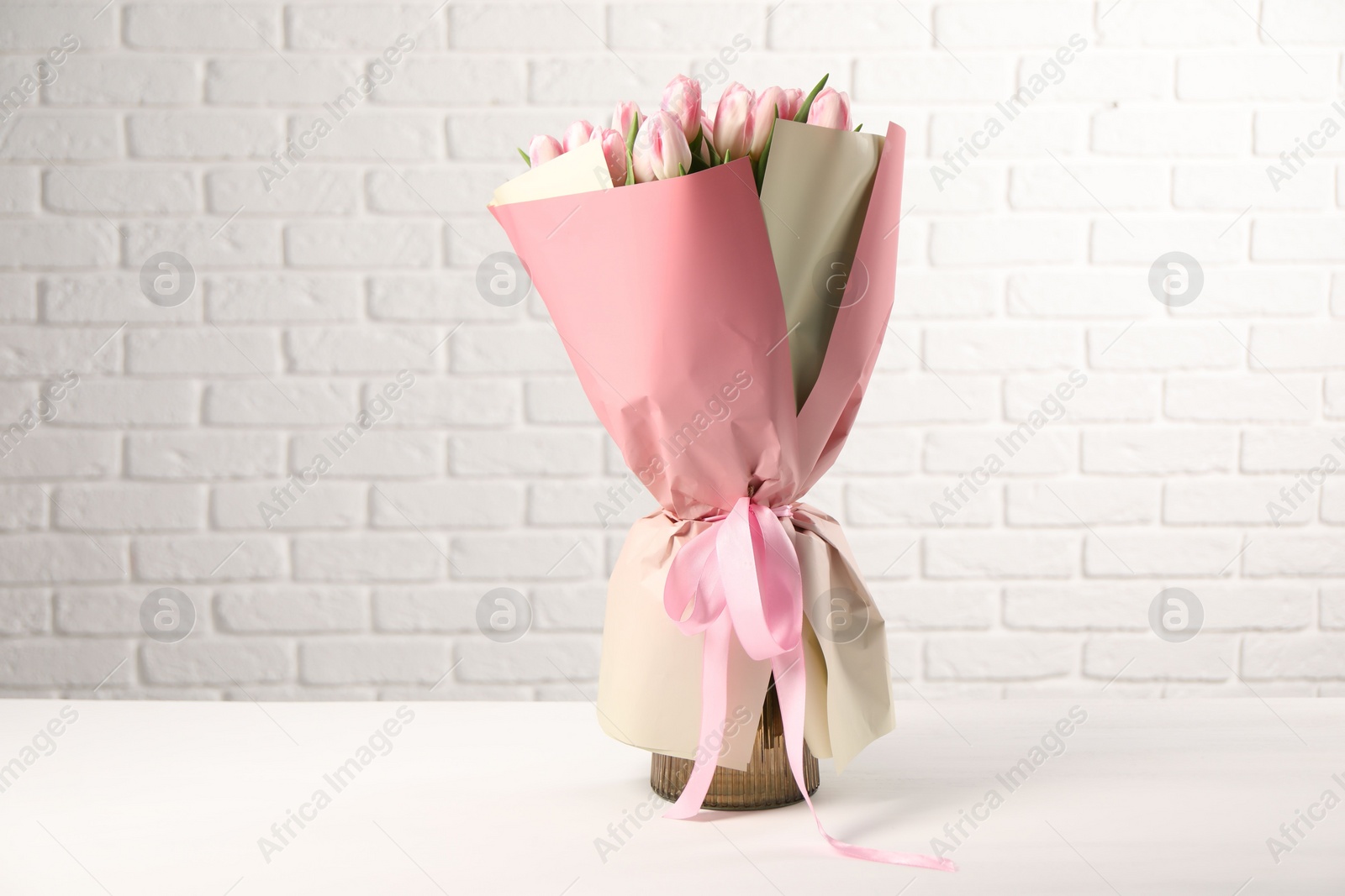 Photo of Beautiful bouquet of fresh pink tulips on table near white brick wall