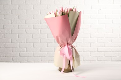 Beautiful bouquet of fresh pink tulips on table near white brick wall