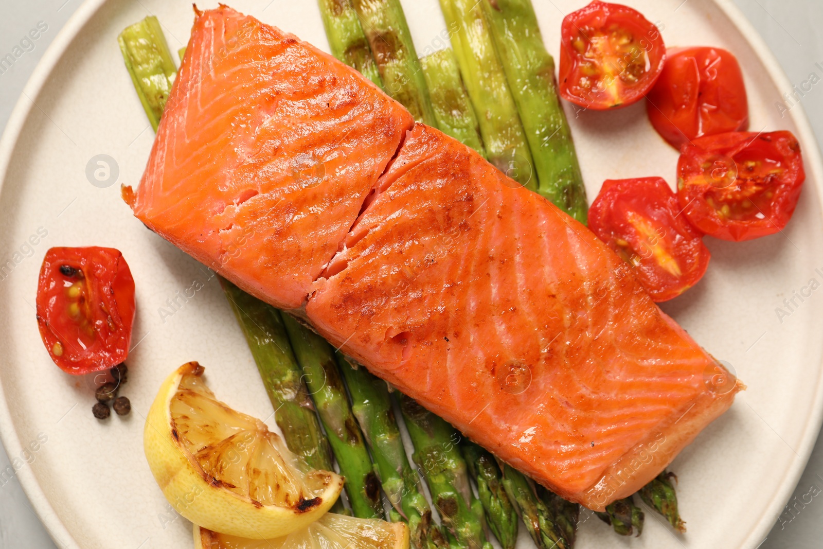 Photo of Tasty grilled salmon with asparagus, tomatoes, spices and lemon on light table, top view