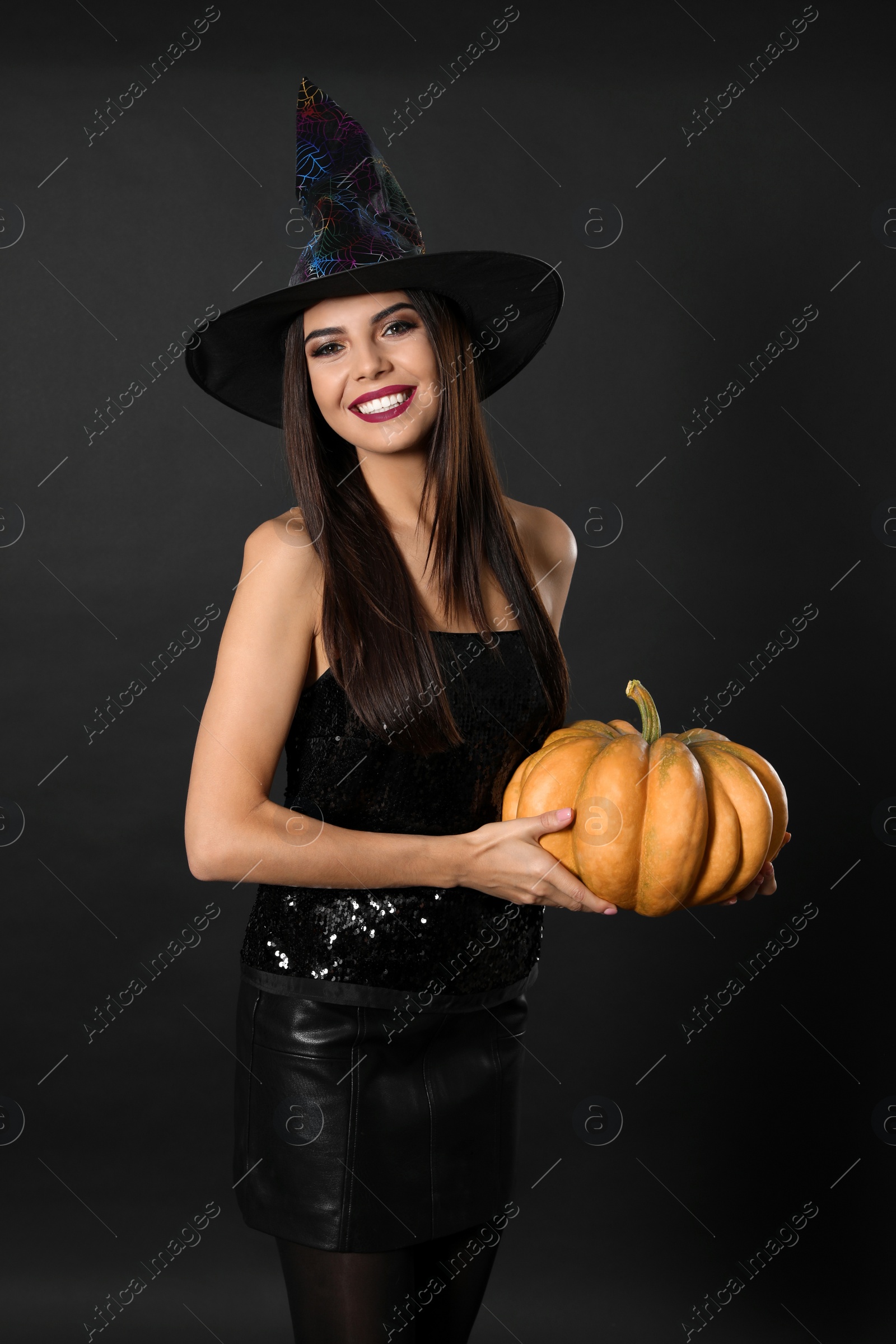 Photo of Beautiful woman wearing witch costume with pumpkin for Halloween party on black background