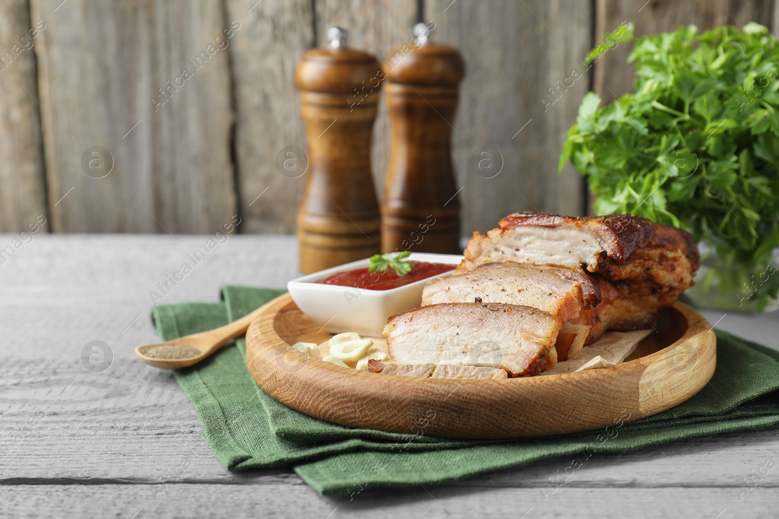 Photo of Pieces of baked pork belly served with sauce on grey wooden table, space for text