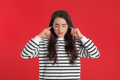 Photo of Emotional young woman covering ears with fingers on red background