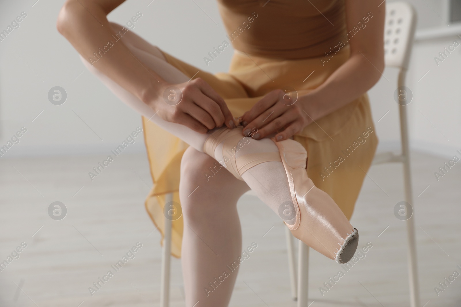 Photo of Ballerina tying pointe shoes in dance studio, closeup