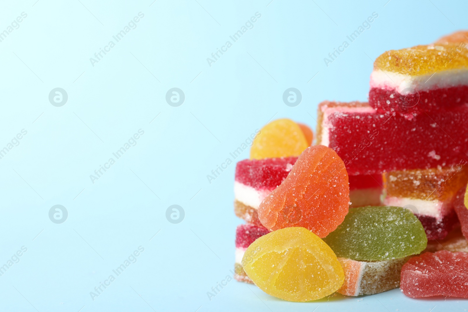 Photo of Pile of delicious bright jelly candies on light blue background, closeup. Space for text