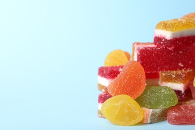 Photo of Pile of delicious bright jelly candies on light blue background, closeup. Space for text