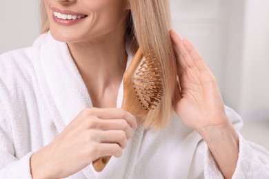 Photo of Woman in robe brushing her hair indoors, closeup