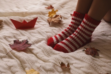 Photo of Woman in warm socks and dry leaves on knitted blanket, closeup