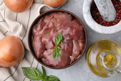 Photo of Bowl with raw chicken liver, basil, peppercorns and onions on light grey table, flat lay