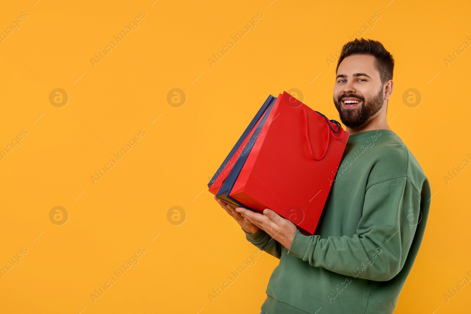 Photo of Happy man with many paper shopping bags on orange background. Space for text