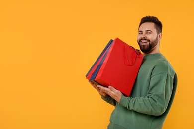 Happy man with many paper shopping bags on orange background. Space for text