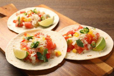 Photo of Delicious tacos with vegetables and lime on wooden table, closeup