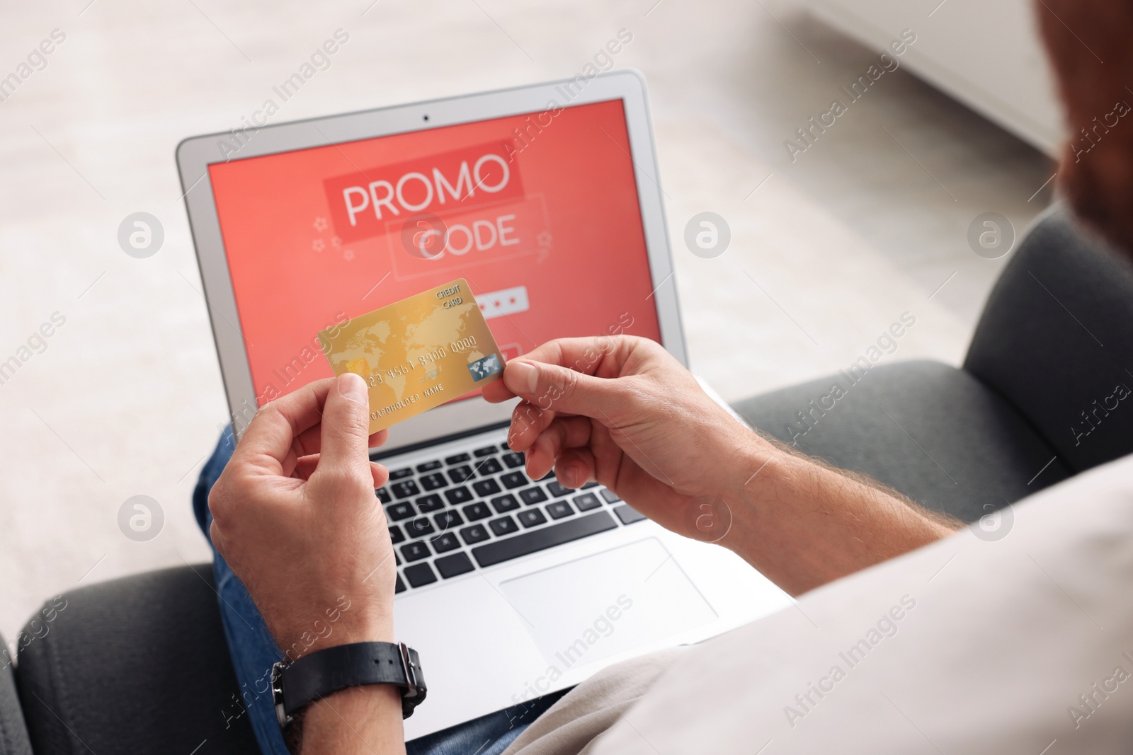 Photo of Man holding laptop with activated promo code and credit card on sofa, closeup