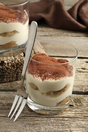 Photo of Delicious tiramisu in glasses and fork on wooden table