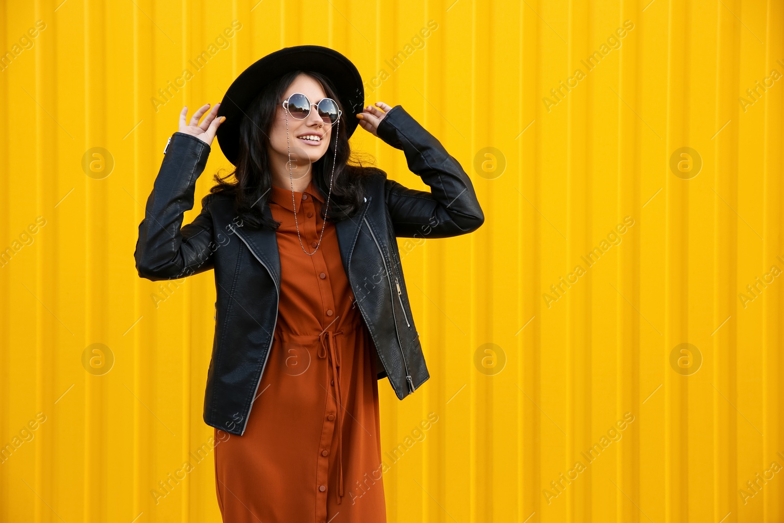 Photo of Beautiful young woman in stylish autumn clothes near yellow fence. Space for text