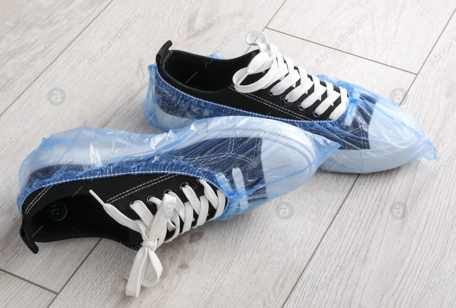 Photo of Sneakers in blue shoe covers on light wooden floor