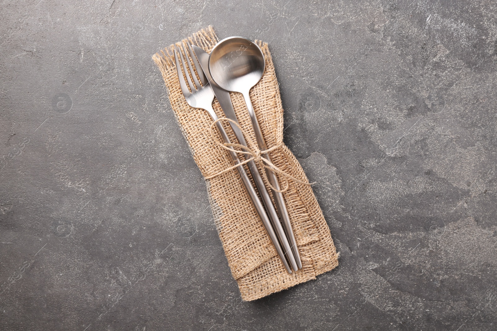 Photo of Set of stylish cutlery and napkin on grey textured table, top view