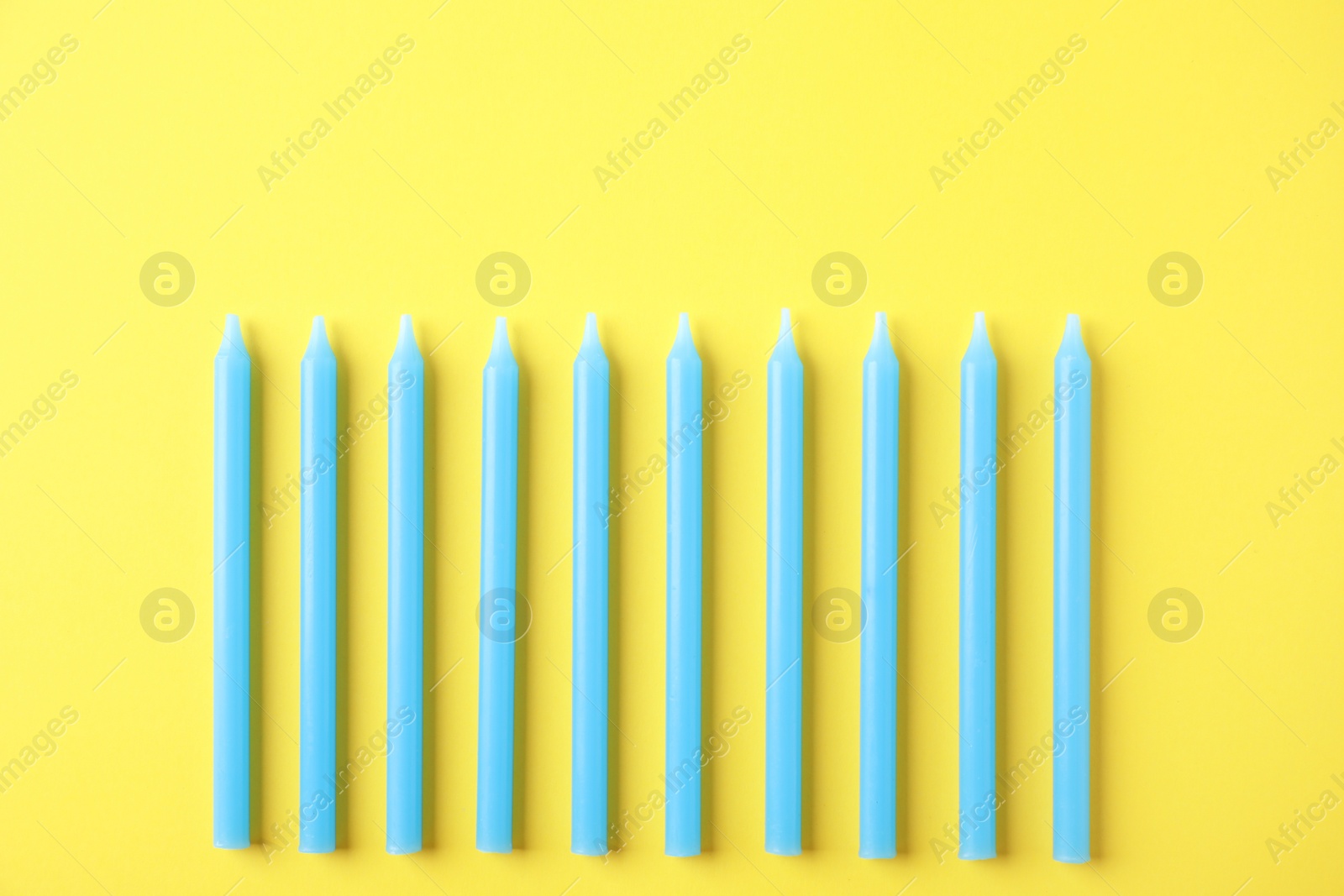 Photo of Blue birthday candles on yellow background, top view
