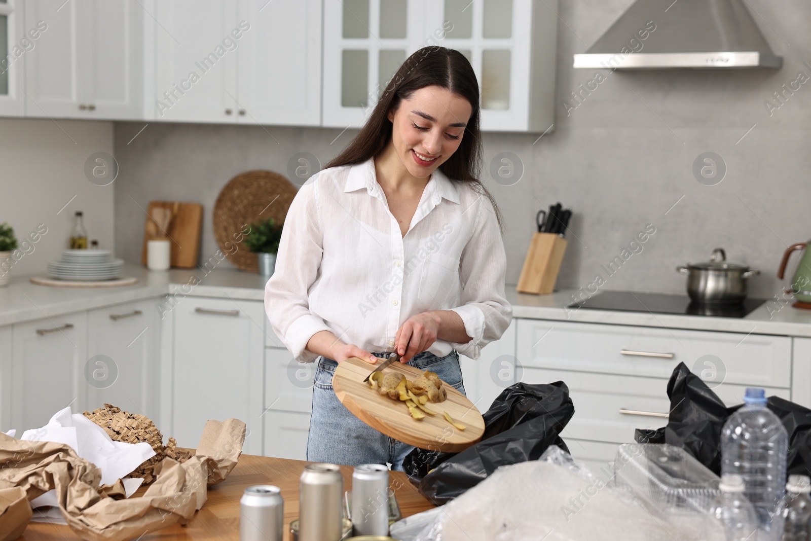 Photo of Garbage sorting. Woman putting food waste into plastic bag at table in kitchen