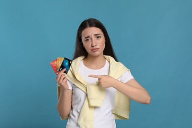 Photo of Confused woman pointing at credit cards on light blue background. Debt problem