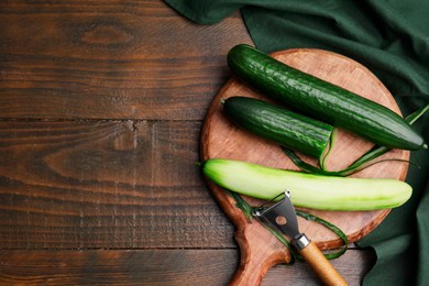 Photo of Fresh cucumbers and peeler on wooden table, top view. Space for text